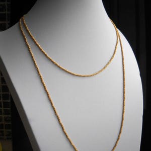 May include: A gold chain necklace with a rope chain design. The necklace is layered on a white mannequin bust.