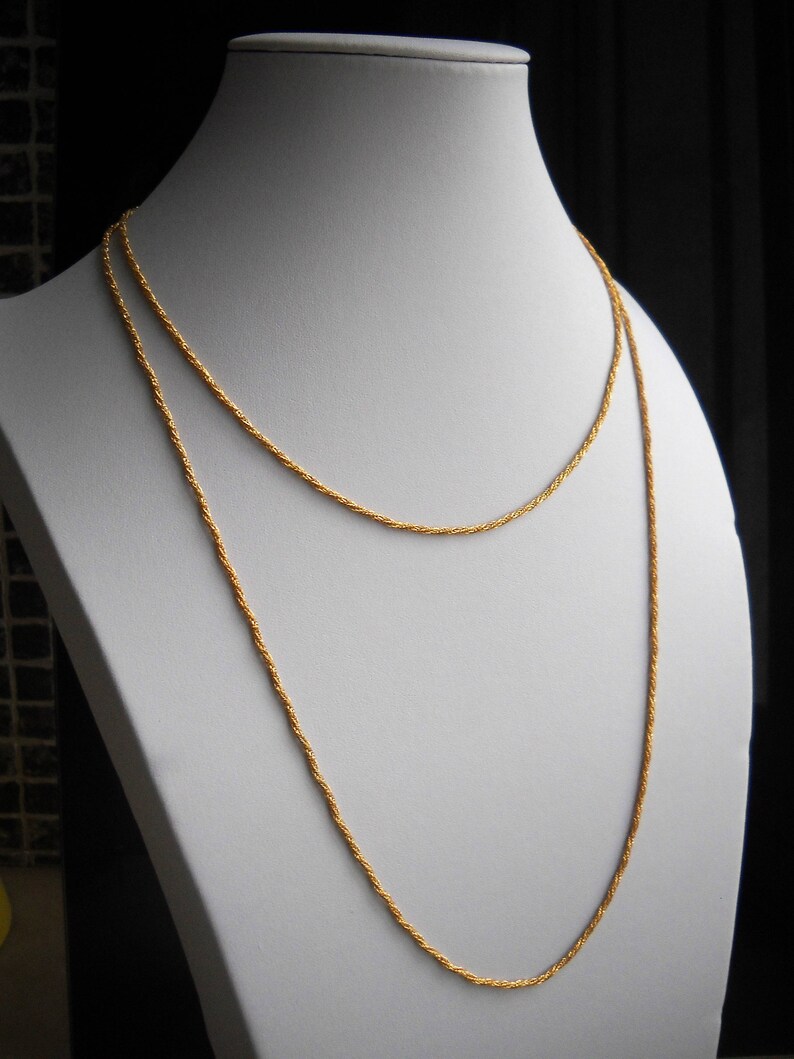 May include: A gold chain necklace with a rope chain design. The necklace is layered on a white mannequin bust.