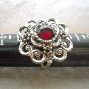 Pode incluir: Um anel de filigrana de prata com uma grande gema vermelha facetada no centro.
