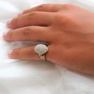 May include: A gold ring with a large oval-shaped clear stone set in the centre. The stone is surrounded by smaller clear stones.