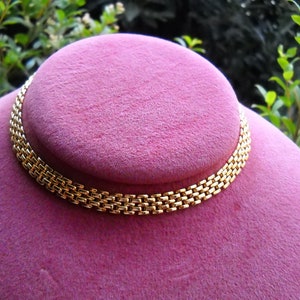 May include: A gold chain necklace with a box link design. The necklace is displayed on a pink velvet stand.