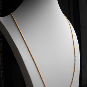 May include: A gold chain necklace on a white mannequin. The chain is a twisted rope design.