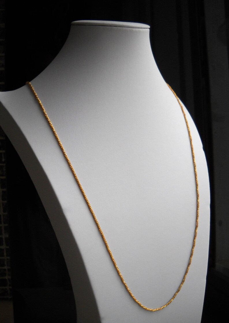 May include: A gold chain necklace on a white mannequin. The chain is a twisted rope design.