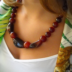 Puede incluir: Una mujer con una camisa blanca y una bufanda estampada con un collar largo de cuentas de color rojo oscuro y negro.