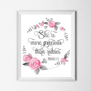 Puede incluir: Una impresión enmarcada en blanco con un diseño de corona floral. La corona está hecha de flores y hojas de acuarela rosa y gris. El texto dentro de la corona dice "Ella es más preciosa que las rubíes" con la referencia bíblica "Proverbios 3:15" debajo.