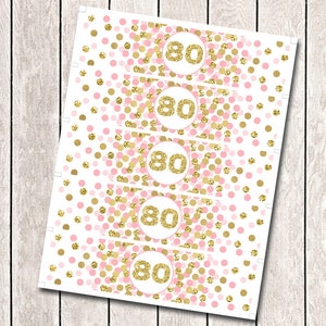 May include: Five pink and gold can cooler labels with the number 80 in gold glitter. The labels have a polka dot pattern.