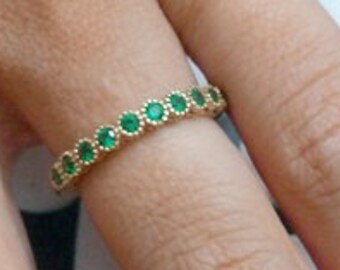 Puede incluir: Un anillo de banda de oro con una fila de pequeñas piedras preciosas redondas verdes.