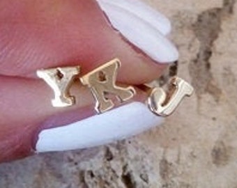 May include: Gold initial letter earrings with the letters Y and K. The earrings are shown on a finger with white nail polish.