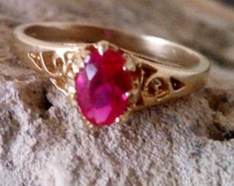 May include: A gold ring with a delicate filigree design and a large, oval-shaped ruby gemstone.