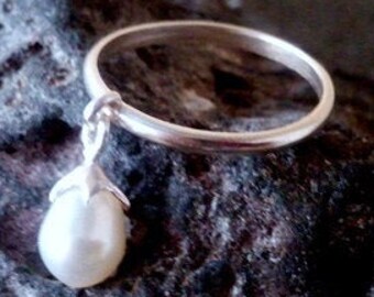 May include: A silver ring with a dangling pearl charm. The ring is simple and elegant, and the pearl is white and lustrous.