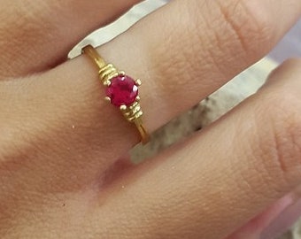 Può includere: Un anello d'oro con una singola pietra preziosa rossa incastonata al centro.