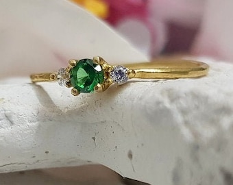 Puede incluir: Un anillo de oro con una piedra preciosa verde y dos piedras blancas más pequeñas.