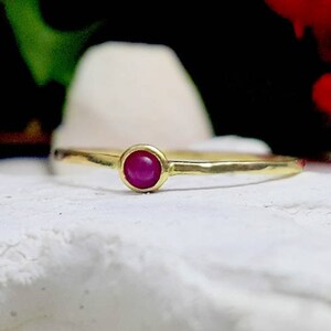 May include: A simple gold band ring with a single, round, pink gemstone set in the center.
