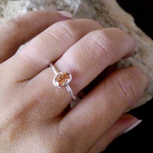 K&ouml;nnte beinhalten: Ein silberner Ring mit einem kleinen, ovalen, orangefarbenen Edelstein.