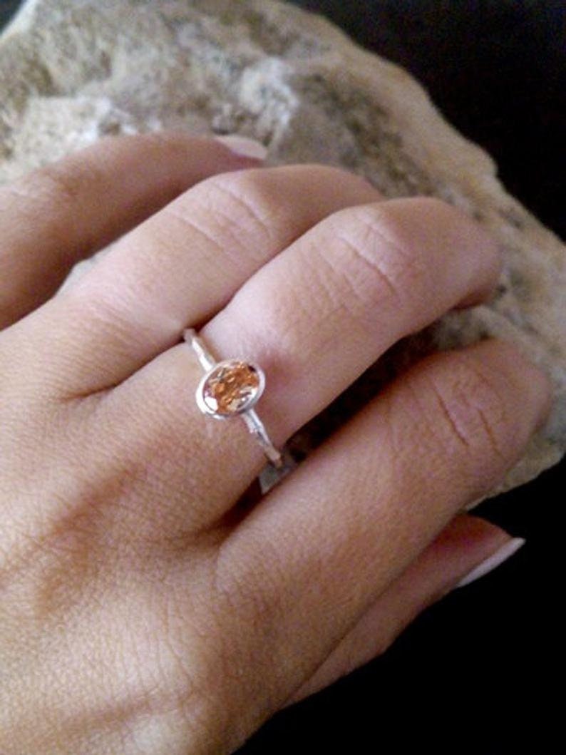 K&ouml;nnte beinhalten: Ein silberner Ring mit einem kleinen, ovalen, orangefarbenen Edelstein.