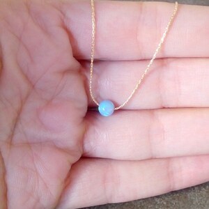 May include: A delicate gold chain necklace with a single light blue opal gemstone pendant.