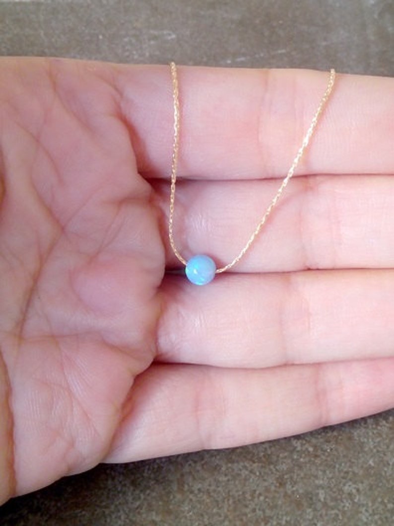 May include: A delicate gold chain necklace with a single light blue opal gemstone pendant.