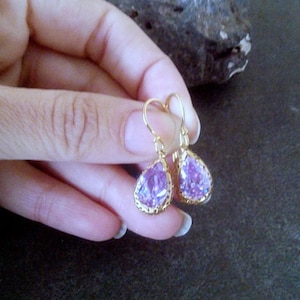 May include: A pair of gold dangle earrings with teardrop-shaped purple gemstones.