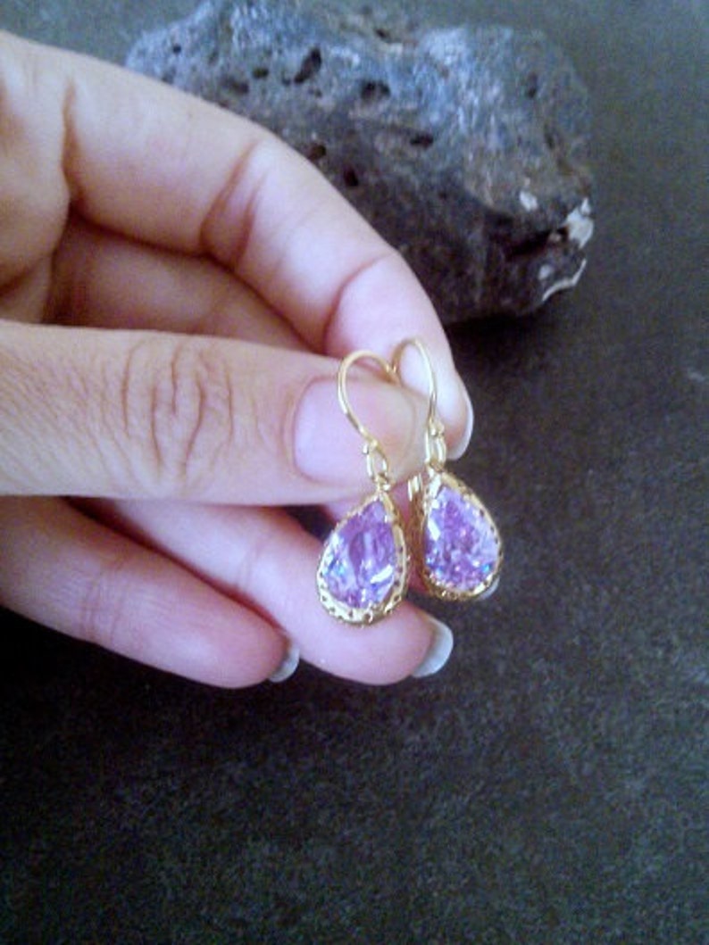 May include: A pair of gold dangle earrings with teardrop-shaped purple gemstones.