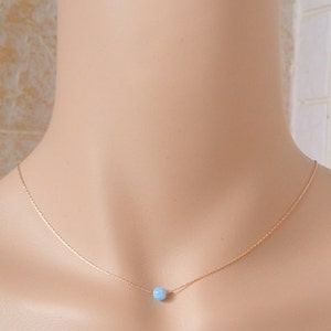 May include: A delicate gold chain necklace with a single light blue opal gemstone pendant.