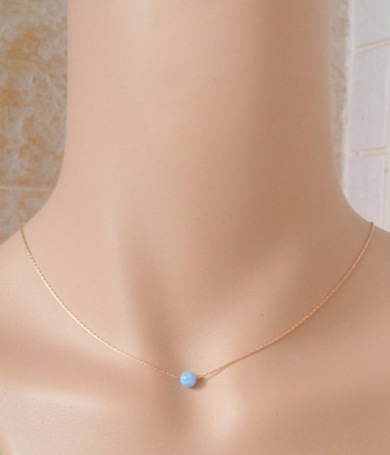May include: A delicate gold chain necklace with a single light blue opal gemstone pendant.