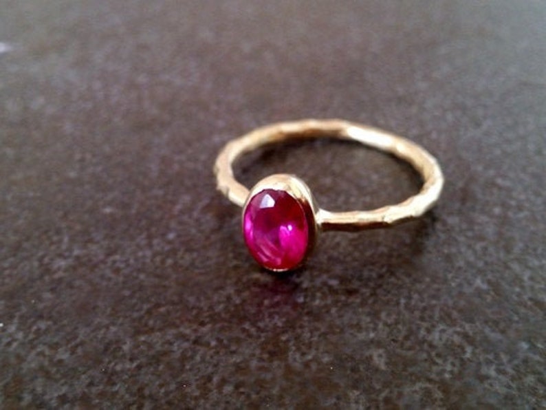 K&ouml;nnte beinhalten: Ein goldener Ring mit einer strukturierten Band und einem leuchtend pinkfarbenen ovalen Edelstein.