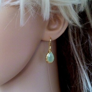 May include: Gold teardrop earrings with a light green gemstone.