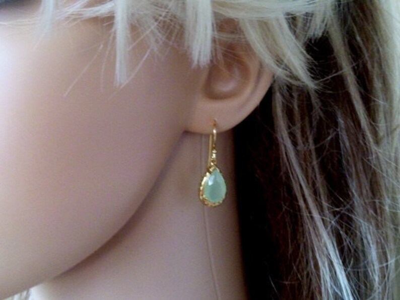 May include: Gold teardrop earrings with a light green gemstone.