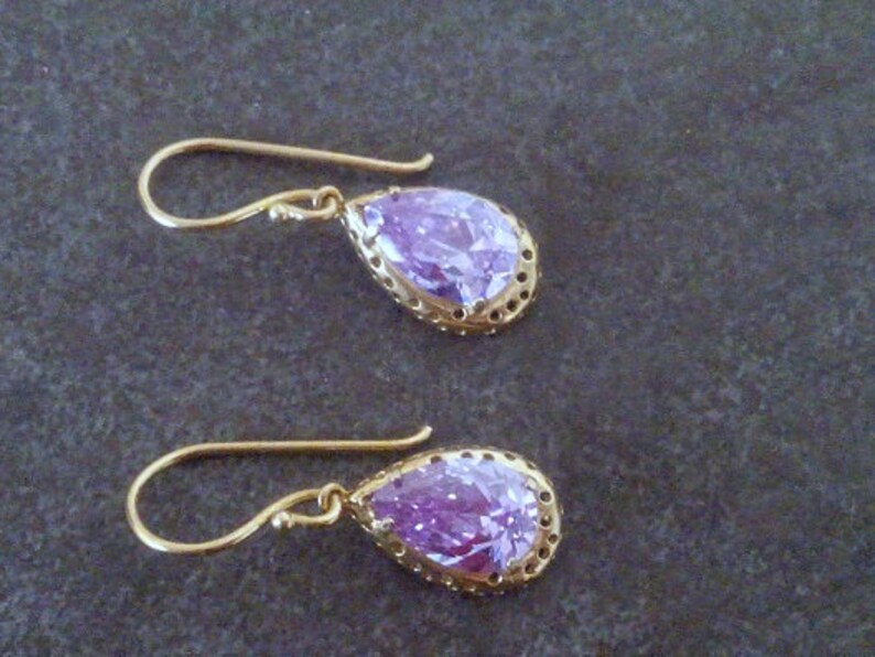 May include: A pair of gold earrings with a teardrop-shaped purple gemstone set in a gold filigree frame.