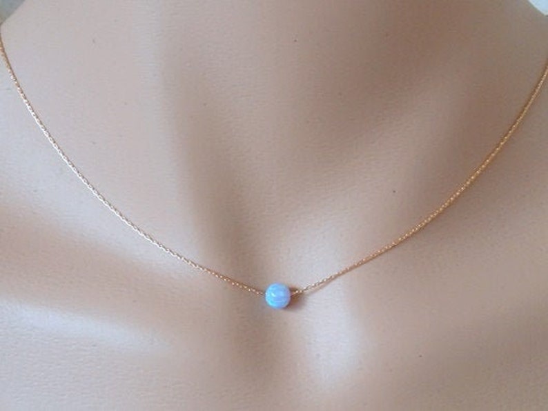 May include: A delicate gold chain necklace with a single light blue opal bead pendant.