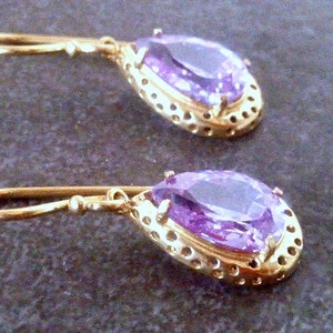 May include: A pair of gold earrings with purple teardrop-shaped stones set in a gold filigree design.