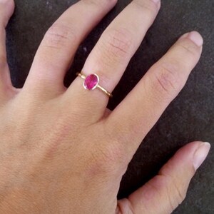 K&ouml;nnte beinhalten: Ein goldener Ring mit einem leuchtend pinkfarbenen ovalen Edelstein.