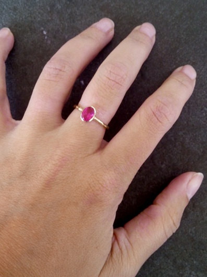 K&ouml;nnte beinhalten: Ein goldener Ring mit einem leuchtend pinkfarbenen ovalen Edelstein.