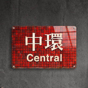 Puede incluir: Un letrero de pared rectangular con un fondo de patrón de mosaico rojo, con los caracteres chinos para Central y la palabra inglesa Central impresos en blanco. El letrero está montado con cuatro soportes metálicos plateados.
