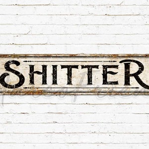 May include: A rustic metal sign with a distressed white background and black lettering that reads "SHITTER".