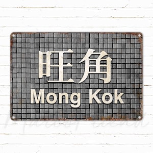 May include: A vintage-style metal sign with a distressed finish. The sign features the Chinese characters for "Mong Kok" and the English translation "Mong Kok" in white lettering on a gray tiled background.