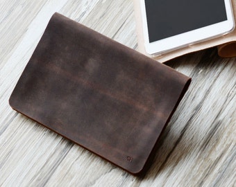 May include: A brown leather tablet case with a stand feature. The case is folded to create a stand for the tablet. The tablet is white with a black screen.