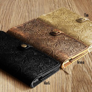 Puede incluir: Tres diarios de cuero con patrones florales en relieve en negro, marr&oacute;n y beige. Los diarios tienen un cierre de broche y est&aacute;n dispuestos en una pila.
