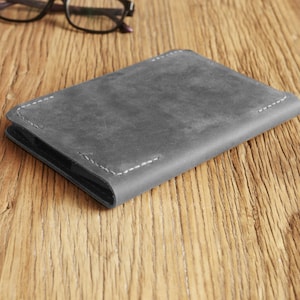 Puede incluir: Una cartera de cuero gris con un borde cosido.
