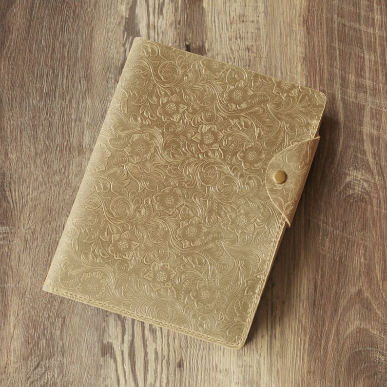 Puede incluir: Un diario de cuero dorado con un dise&ntilde;o en relieve floral y un cierre de bot&oacute;n.