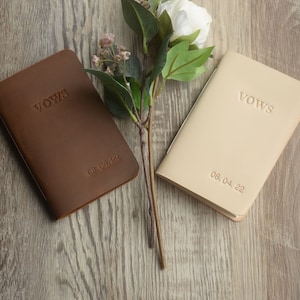 May include: Two leather-bound vow books, one brown and one beige, with the word "Vows" embossed on the front. The date is embossed on the bottom of each book: 08.04.22 and 06.04.22.
