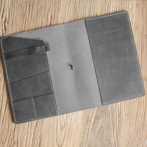 May include: A grey leather notebook with a flap closure and multiple pockets on the inside cover.