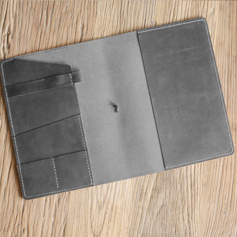 May include: A grey leather notebook with a flap closure and multiple pockets on the inside cover.