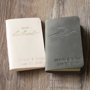 May include: Two leather-bound journals, one in beige and one in gray, with the words "To My Husband" and "To My Wife" embossed on the covers. Both journals have the names "Michele & Simon" and the date "June 22, 2024" printed on the bottom.