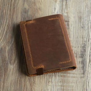 Peut inclure: Une couverture de carnet en cuir marron avec une bordure cousue et une fermeture &agrave; sangle.