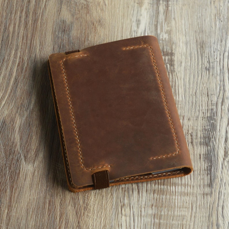 Peut inclure: Une couverture de carnet en cuir marron avec une bordure cousue et une fermeture &agrave; sangle.