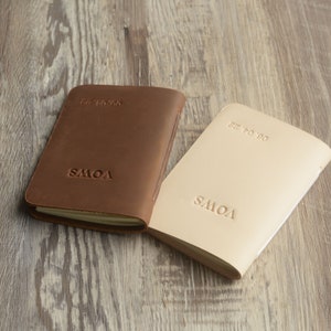 May include: Two leather-bound journals with the word "SMOV" embossed on the front. The journal on the left is brown and the journal on the right is beige.