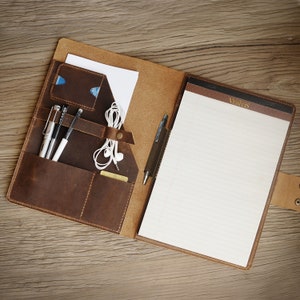 May include: A brown leather portfolio with a notepad, pen, and other office supplies. The notepad has the word "Veritas" printed on the top.