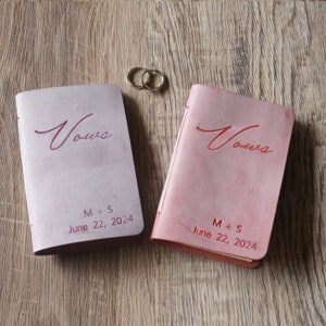 Peut inclure: Deux livres de v&oelig;ux reli&eacute;s en cuir rose avec le mot "V&oelig;ux" en relief sur la couverture. Les livres sont personnalis&eacute;s avec les initiales "M + S" et la date "22 juin 2024".