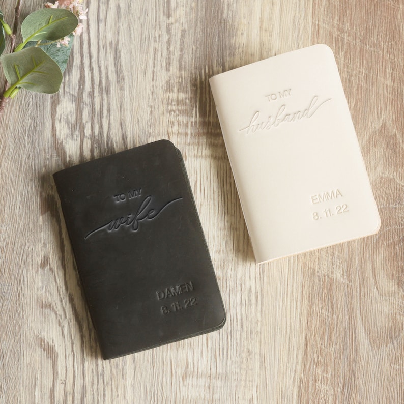 May include: Two small black and white leather-bound journals with the words "To my wife" and "To my husband" embossed on the covers. The journals are personalized with the names "Damen" and "Emma" and the date "8.11.22".